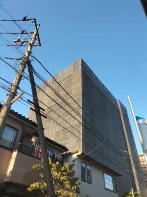 埼玉県越谷市の大規模修繕工事現場。仮設足場の架設が完了し、建物全体をメッシュシートで養生した様子。